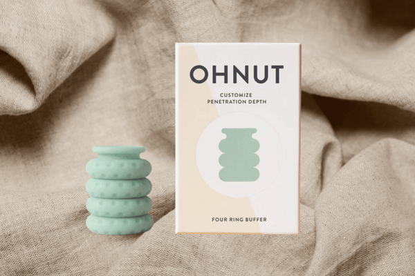 Ohnut depth limiting rings next to a box resting on a sheet representing the bedroom - to reduce pain with sex