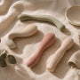 Flat-lay of four smooth silicone vibrators in blush, cream and sage tones on soft linen with a eucalyptus sprig