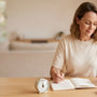 Woman at home noting bladder retraining times in a journal with a glass of water and a timer on the table