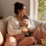 A new mother sitting on a linen sofa by a window in soft morning light, gently cradling her sleeping newborn, calm and unhurried at home