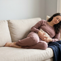 Australian woman resting on a sofa at home holding a warm heat pack against her lower abdomen to ease pelvic pain