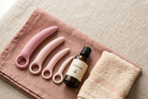Graduated set of silicone vaginal dilators arranged small to large on linen beside lubricant and a towel for at-home use