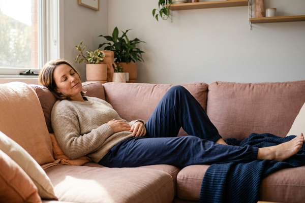 Australian woman reclining calmly on a linen sofa at home, eyes closed and shoulders relaxed, easing pelvic floor tension