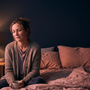 Woman sitting on the edge of her bed by a warm lamp at night holding a mug, awake with nocturia