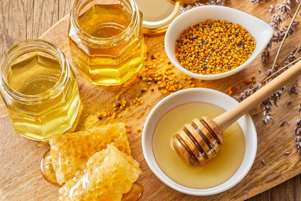 Jars of honey, honeycomb, bee pollen and lavender on a wooden board, reflecting the natural ingredients in Olive & Bee intimate cream