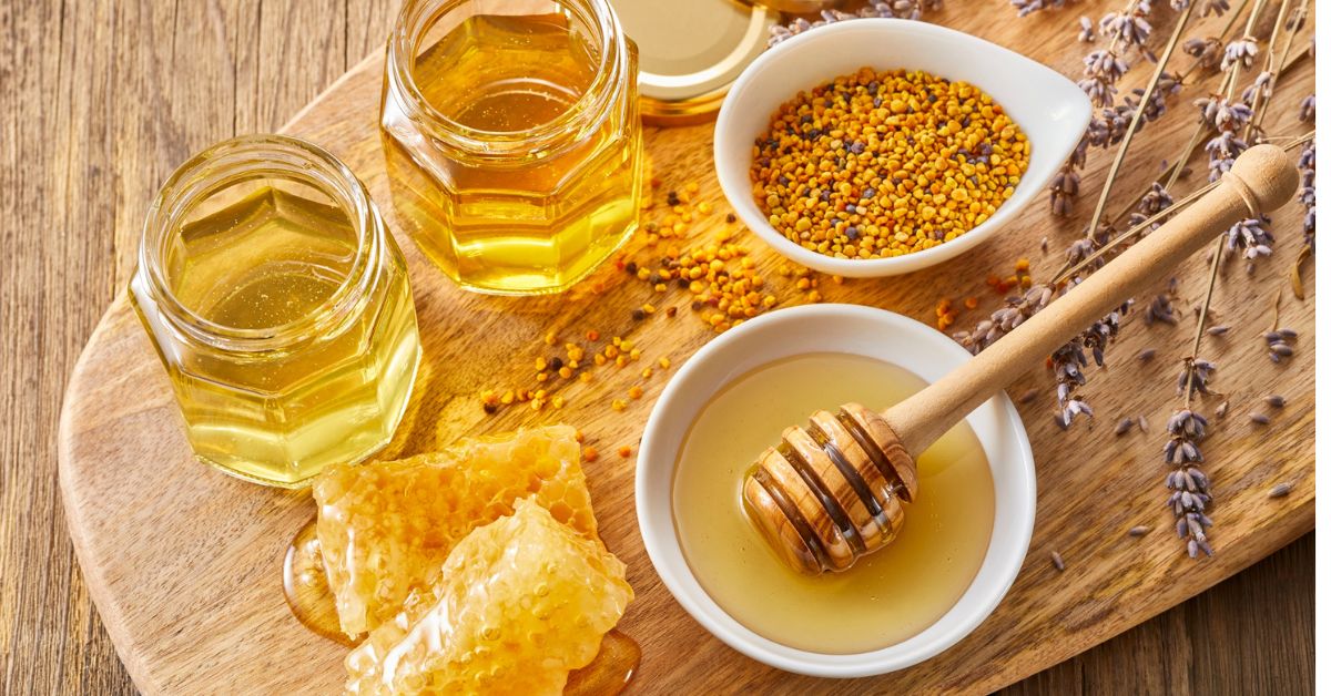 Jars of honey, honeycomb, bee pollen and lavender on a wooden board, reflecting the natural ingredients in Olive & Bee intimate cream