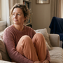 Woman resting on her sofa with knees drawn up by a window at home, reflecting on pelvic pain symptoms