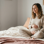 Pregnant woman resting calmly on a bed in soft natural light with her hands on her bump, preparing for birth