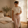 Woman six weeks postpartum at home in high-waisted compression leggings, a folded postpartum support band on the bed beside her