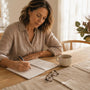 Woman at a timber dining table in morning light writing a list of questions in a notebook before a prolapse surgery consult