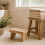 Timber toilet footstool and folded towels in a bright bathroom, set up for easier bowel emptying