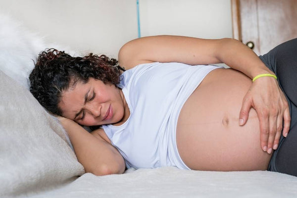 Pregnant woman lying on her side in bed with a hand on her belly, easing pelvic girdle pain