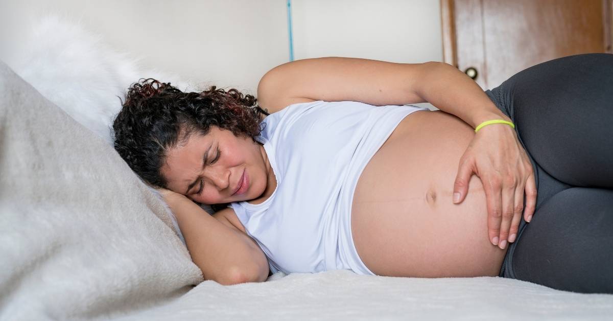 Pregnant woman lying on her side in bed with a hand on her belly, easing pelvic girdle pain