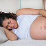 Pregnant woman lying on her side in bed with a hand on her belly, easing pelvic girdle pain