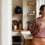Woman holding a glass of water by a sunlit kitchen window at home, calm — urge incontinence versus stress incontinence