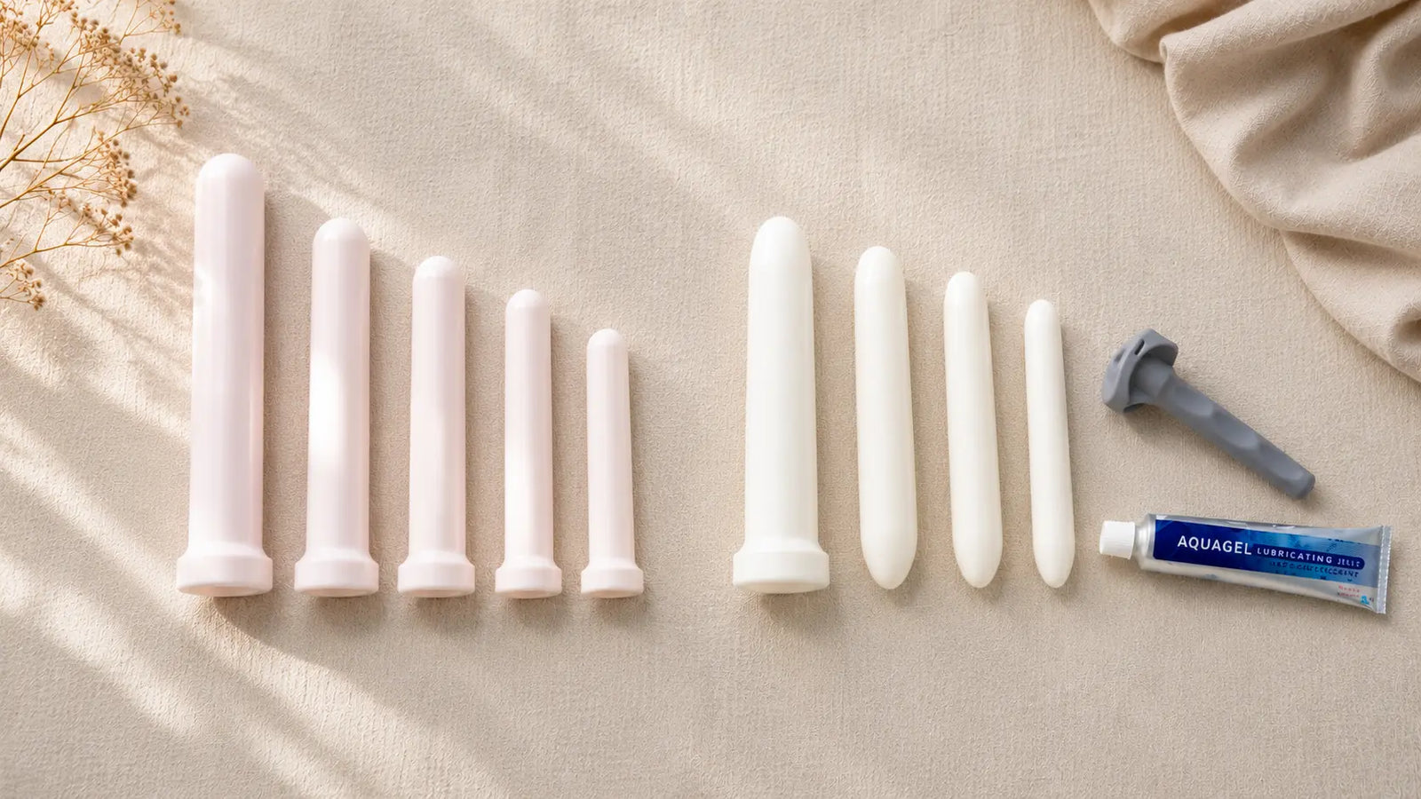Amielle Comfort and Amielle Care vaginal dilator sets compared side by side — graduated tapered and non-tapered plastic dilators with universal locking handle and Aquagel lubricant on cream linen.
