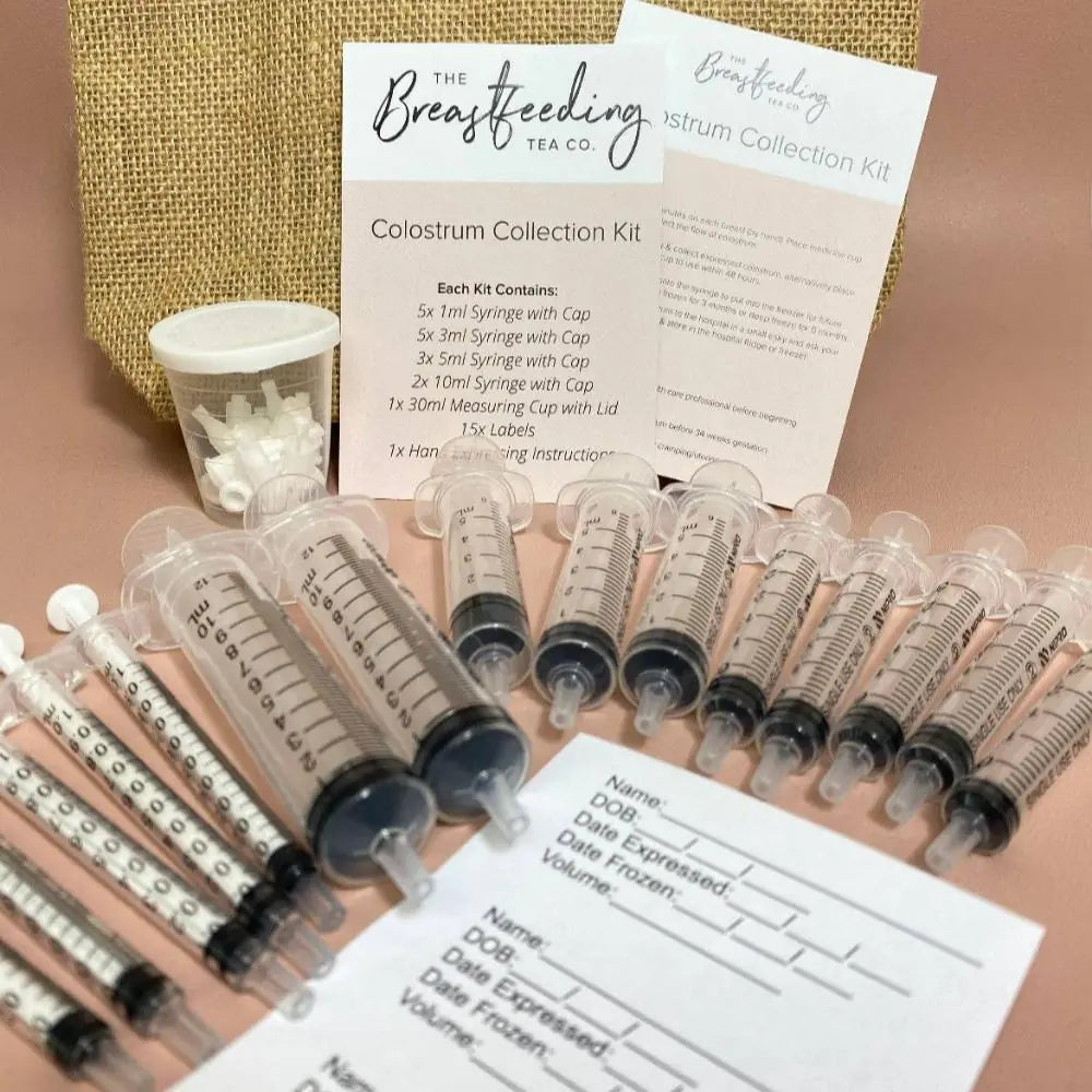 The Breastfeeding Tea Co Colostrum Collection Kit is shown on a light surface, neatly arranged with multiple syringes, collection labels, caps, instruction sheets, and a branded card.