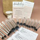 The Breastfeeding Tea Co Colostrum Collection Kit is shown on a light surface, neatly arranged with multiple syringes, collection labels, caps, instruction sheets, and a branded card.