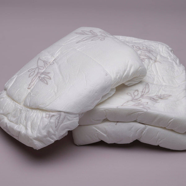 Two Bubba Bump Disposable Postpartum Underwear with floral patterns are folded neatly on a smooth, light purple surface. They feature a quilted design for softness and offer leak-proof protection to keep you comfortable and confident.