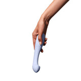 A hand holding the Dame Arc, a G-Spot vibrator by Dame, featuring an ergonomic design with a curved shape in light blue medical-grade silicone. The background is plain white.