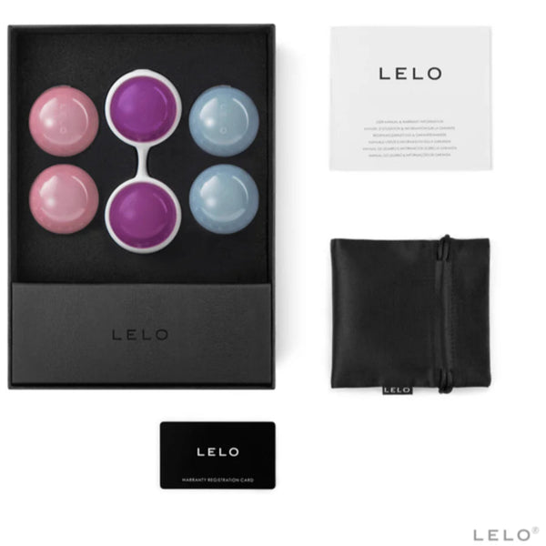 The LELO Beads Plus Pleasure Set by LELO features four Ben Wa balls (two pink, two blue), a purple dual silicone holder, black pouch, warranty card, and instruction booklet for pelvic floor training, all shown on a white background.