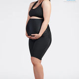 A pregnant woman, dressed in a black SRC Health sports bra and SRC Pregnancy Shorts - Over the Bump, stands with both hands gently cradling her belly. She smiles warmly as she gazes down at her bump. The image features the endorsement of the Australian Physiotherapy Association, indicated by their logo in the upper right corner.