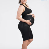 An expectant mother in a black SRC Pregnancy Shorts - Over the Bump and matching sports bra beams as she cradles her baby bump. Standing sideways in black athletic shoes, she demonstrates the pelvic support feature of the SRC Health product. The image is endorsed by the Australian Physiotherapy Association, with their logo visible in the top right corner.