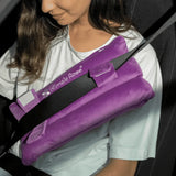 A person seated in a car uses the Intimate Rose Post-Surgery Seat Belt Pillow to enhance comfort after surgery. This cushion, akin to a mastectomy pillow, attaches to the seatbelt and offers pain relief as they rest their arm on it. The individual is wearing a white shirt, with the photograph capturing part of their upper body.