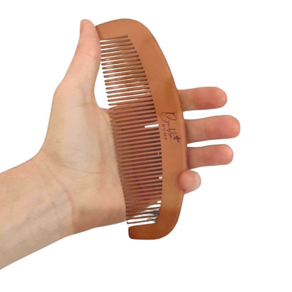 A hand holds the Bubba Bump Labour and Birth Comb, a curved wooden tool with evenly spaced teeth and an acupressure design. Its side features a logo, providing a soothing experience akin to drug-free pain relief.