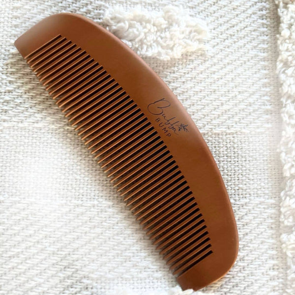A Bubba Bump Labour and Birth Comb, brown with fine teeth and a textured surface, rests on woven fabric. It features the "Bump" logo and is designed as a natural aid for managing labor pain.