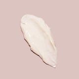 A smear of the creamy, off-white C-Section Mama Cream by Yung Bod is displayed against a blush-colored background. The texture appears smooth and thick, suggesting a rich consistency with natural ingredients designed to soften scars.