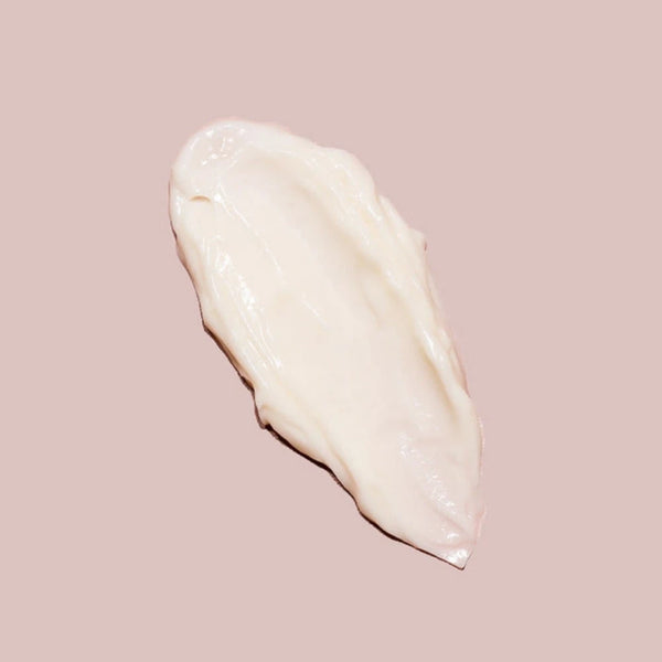 A smear of the creamy, off-white C-Section Mama Cream by Yung Bod is displayed against a blush-colored background. The texture appears smooth and thick, suggesting a rich consistency with natural ingredients designed to soften scars.