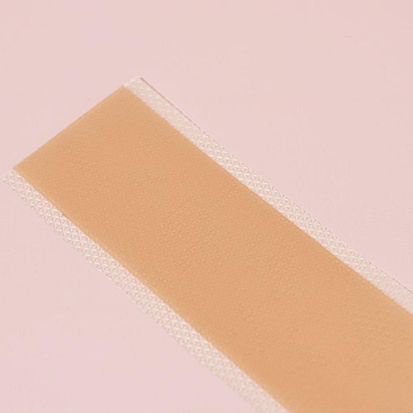 A close-up shot of a single, unwrapped Yung Bod C-Section Silicone Strip with a light brown center strip and white, perforated edges, placed on a light pink surface. Ideal for postpartum scar healing and C-section scar treatment.