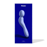 A blue package contains the Dame Com, an ergonomically shaped wand vibrator in gray, featuring a curved design and flexible neck. The packaging prominently showcases the Dame brand name against a dark blue background, promising those signature rumbly vibrations for enhanced pleasure.