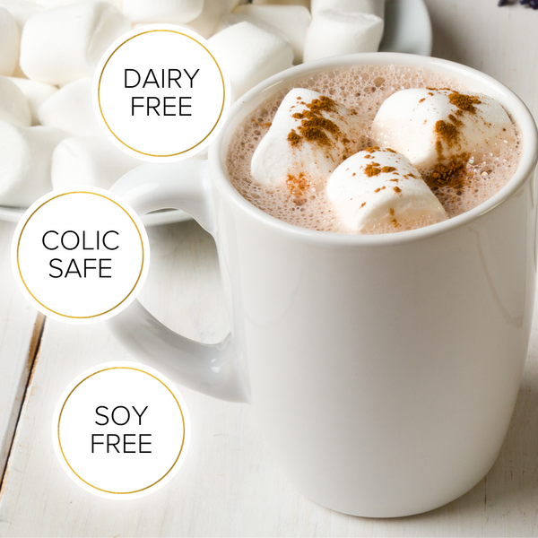 A steaming mug of Lactation Hot Chocolate with Collagen from The Breastfeeding Tea Co topped with marshmallows and a sprinkle of cinnamon. The text around the image indicates the beverage is dairy-free, soy-free, and colic-safe. Made with organic cacao powder, it supports breastmilk supply. In the background, a bowl filled with marshmallows is partially visible.
