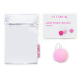 A white drawstring pouch, an Intimina Laselle Kegel Exercisers user manual, and a round pink case—ideal for pelvic floor muscle training—are neatly displayed on a white background.