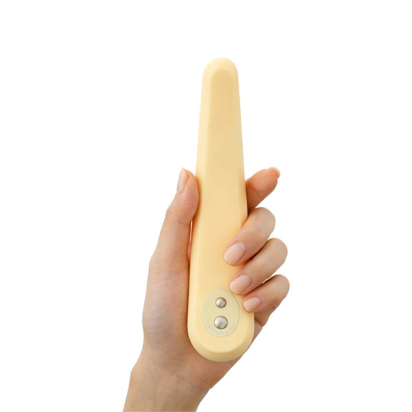 A hand holds the Iroha Mikazuki, a gentle slim vibrator for beginners by Iroha, featuring a beige, elongated oval design with two metal buttons and crafted from body-safe silicone, shown against a white background.