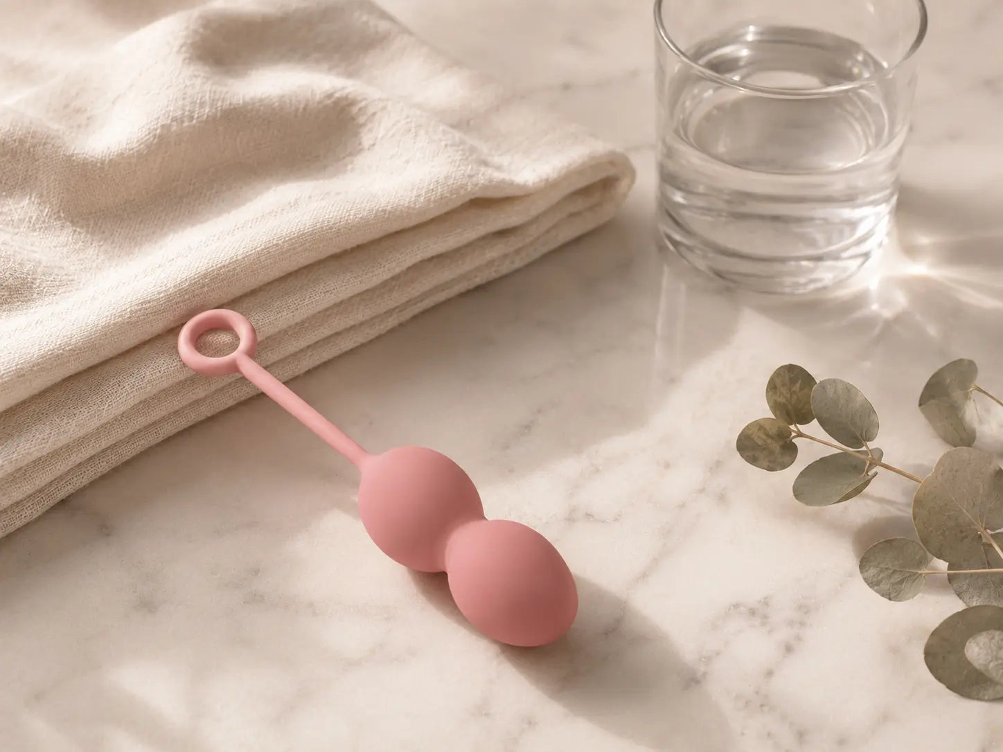 Single pink kegel ball on marble beside a folded towel and eucalyptus sprig — when kegel balls aren't the right pelvic floor training tool