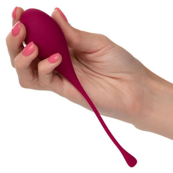 A person's hand holds a small, purple object from the Calexotics Kegel Weights 5-Piece Set, featuring a long, flexible tail for Kegel training. The person's nails are painted pink.