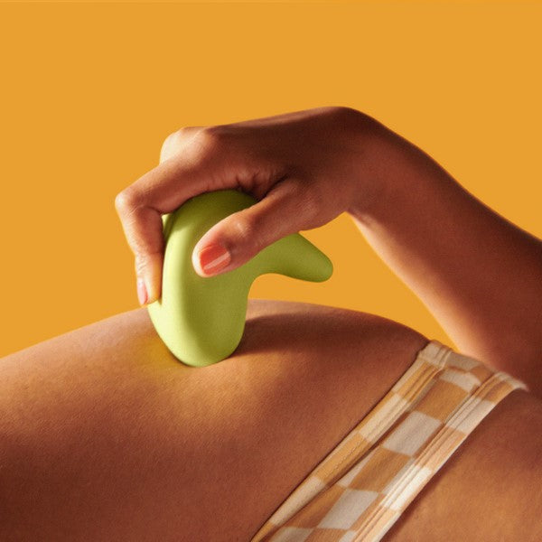A hand holds The Pelvic People's Kiwi Vibrating Pelvic Massager, easing pressure on a person's back as they relax in a checkered outfit against an orange backdrop.