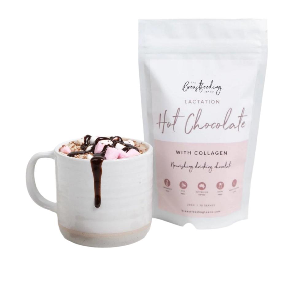 A white mug filled with hot chocolate topped with marshmallows and a chocolate drizzle sits next to a white, resealable bag labeled "Lactation Hot Chocolate with Collagen" by The Breastfeeding Tea Co. Made with organic cacao powder, the product is promoted as nourishing and supportive of breastmilk supply.