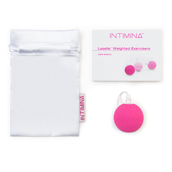 Displayed on a white background are a white drawstring pouch, user manual, and the Intimina Laselle Kegel Exercisers—round pink weighted silicone devices with loops designed to strengthen pelvic floor muscles.