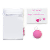 A white pouch, user manual, and pink round Intimina Laselle Kegel Exerciser with a white string on a white background—ideal for strengthening pelvic floor muscles with Intimina's Laselle Kegel Exercisers.