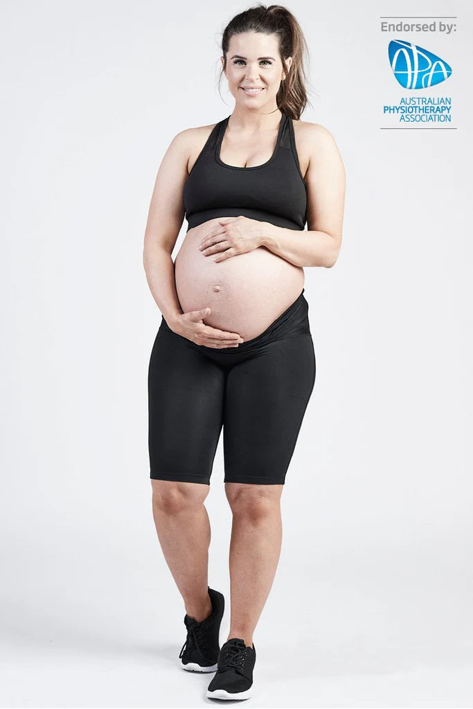 A pregnant woman stands, smiling at the camera while wearing a black sports bra and the SRC Maternity Shorts by SRC Health. She cradles her baby bump with both hands. The image is endorsed by the Australian Physiotherapy Association, whose logo appears in the top right corner.