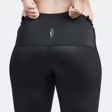 A person is shown from the back, wearing black, high-waisted SRC Maternity Shorts and a matching sports bra. They are pulling up the sides of the shorts with both hands. There is a small green SRC Health logo on the back of these maternity compression shorts designed for pelvic support during pregnancy.