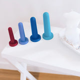 The Bien Silicone Vaginal Dilators - Medium Set from BIEN Australia, featuring an array of four vibrant dilators crafted from medical-grade silicone and available in graduated sizes, is elegantly arranged on a white table next to a decorative tray holding a torso-shaped candle, a small bottle, and rings. This setup is placed on a wooden floor against a white wall.