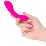 A hand with pink-painted nails holds a small, curved, pink silicone The Mini Swan Wand by Swan. The background is white.