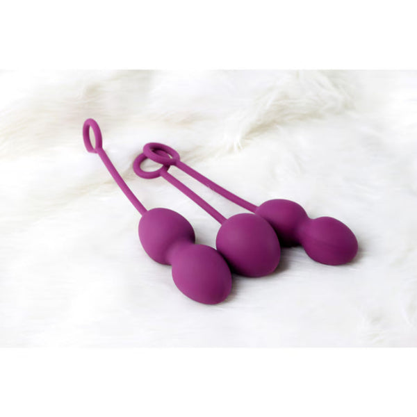 Three purple Intimina Laselle weighted silicone Kegel exercisers with retrieval loops rest on a soft, white, furry surface—ideal for pelvic floor strengthening.