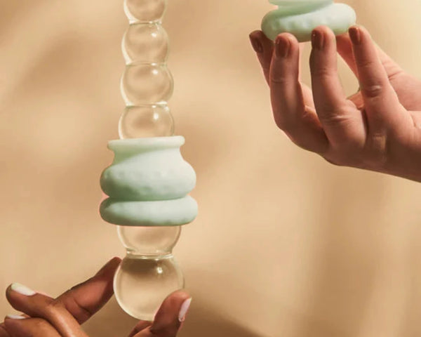 Mint green Ohnut depth-limiting buffer rings stacked on a clear glass dilator while a hand holds an extra ring — demonstrates how Ohnut sets penetration depth during sex. Sold in Australia by Blossom Pelvic Health, a physio-led pelvic store.