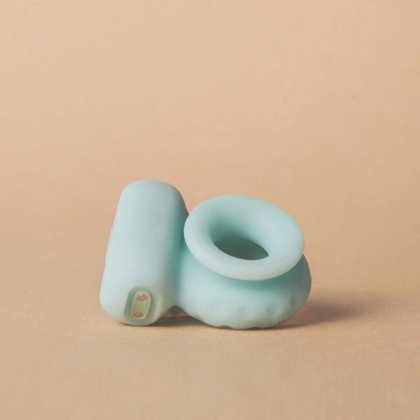 Set against a beige backdrop, the Ohnut Vibrating Ring by The Pelvic People features a light blue silicone design with a cylindrical shape, hollow center, and a small protrusion on one end, providing pain relief and enhanced pleasure.